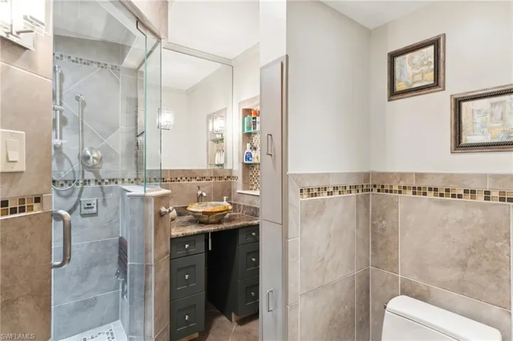 Bathroom featuring tile patterned floors, vanity, tile walls, toilet, and a shower with shower door