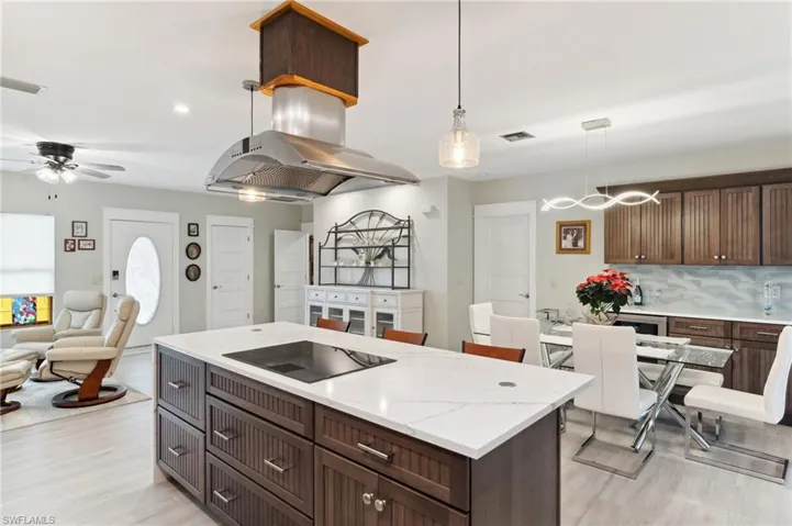 Kitchen with decorative backsplash, black electric stovetop, ceiling fan, decorative light fixtures, and light hardwood / wood-style floors
