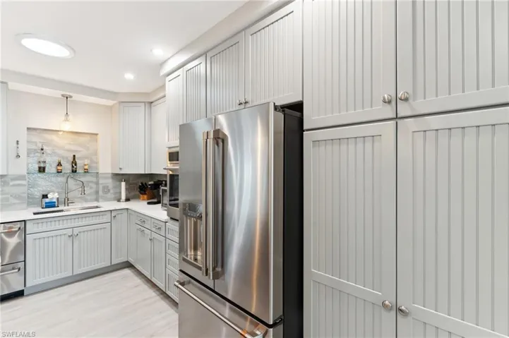 Kitchen with pendant lighting, sink, decorative backsplash, light wood-type flooring, and stainless steel appliances