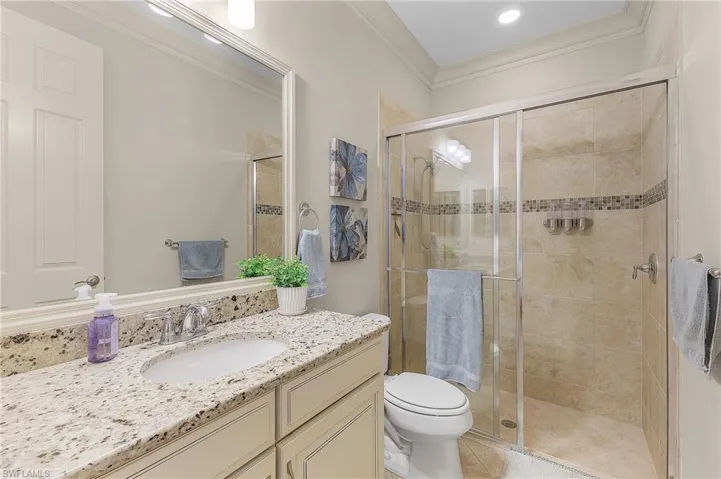 Bathroom featuring a glass-enclosed shower with tile surround, a single vanity with stone countertop, and a built-in mirror