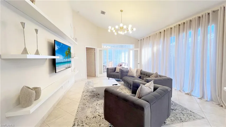 Living area featuring light tile patterned flooring, visible vents, high vaulted ceiling, and a notable chandelier