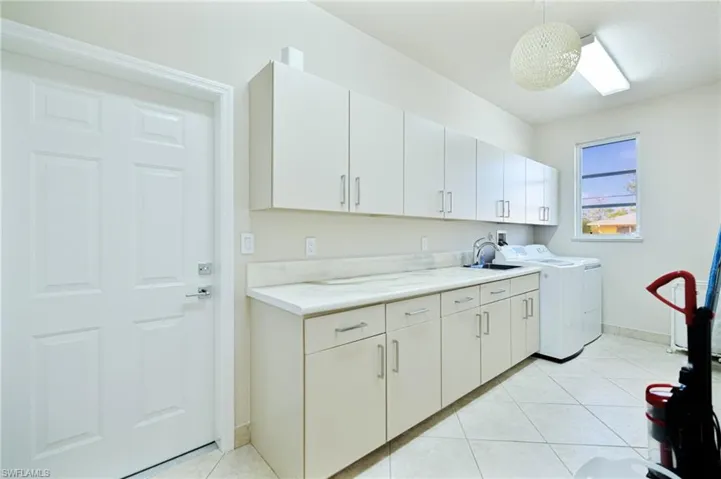 Washroom with a sink, washing machine and dryer, light tile patterned floors, baseboards, and cabinet space