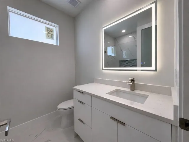 Contemporary bathroom featuring a white vanity with integrated sink, a brushed nickel faucet, and a backlit LED mirror