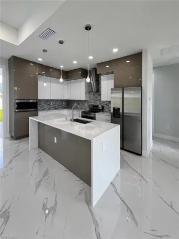 Modern kitchen featuring a waterfall island, stainless steel appliances, sleek cabinetry, pendant lighting, and large format tile flooring