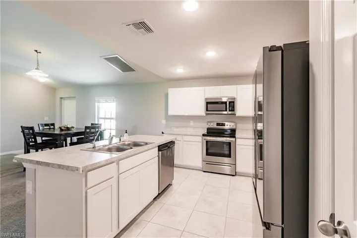 Kitchen with white cabinets, sink, hanging light fixtures, an island with sink, and stainless steel appliances