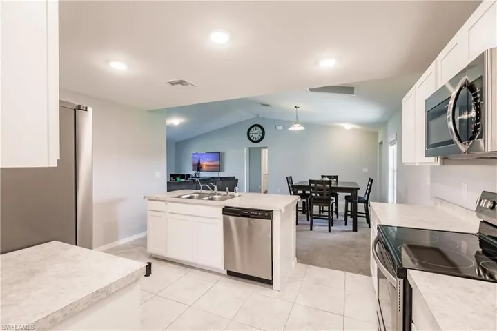 Kitchen featuring vaulted ceiling, light tile patterned floors, decorative light fixtures, white cabinetry, and stainless steel appliances