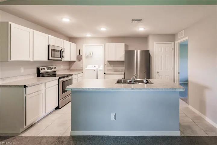 Kitchen with sink, separate washer and dryer, an island with sink, white cabinets, and appliances with stainless steel finishes