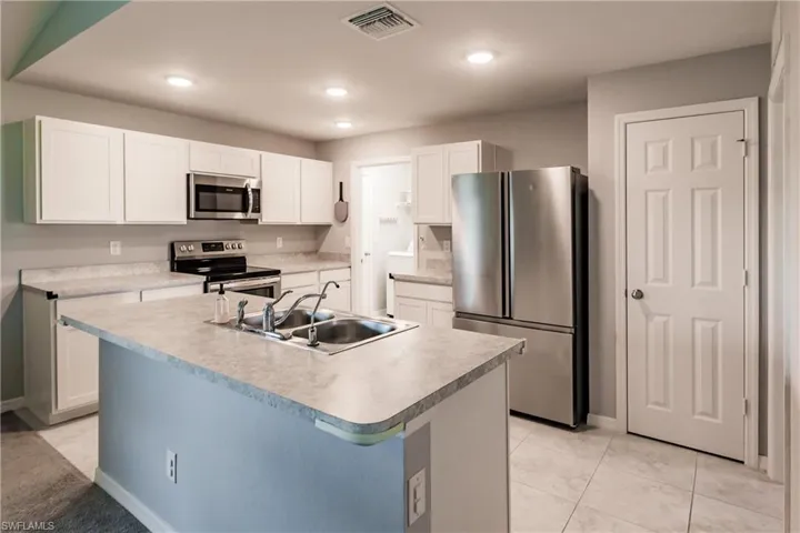 Kitchen featuring sink, light tile patterned flooring, a kitchen island with sink, white cabinets, and appliances with stainless steel finishes