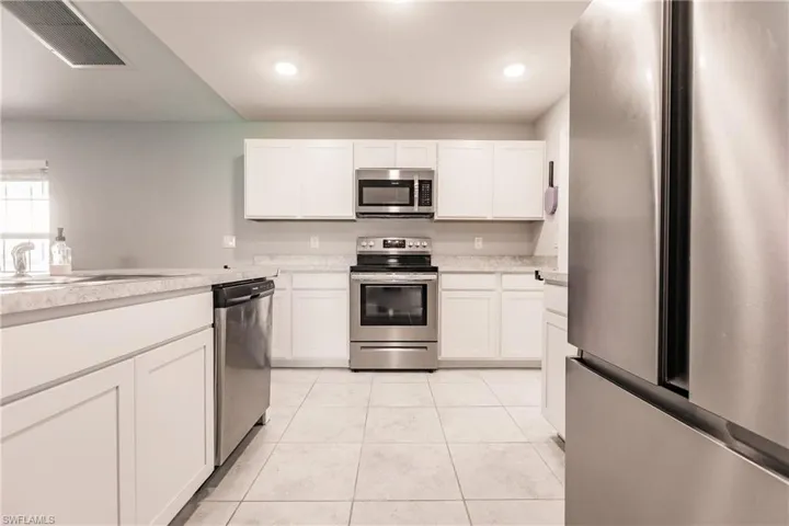Kitchen featuring sink, white cabinets, stainless steel appliances, and light tile patterned floors