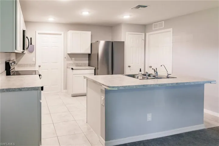 Kitchen with appliances with stainless steel finishes, sink, white cabinetry, and an island with sink