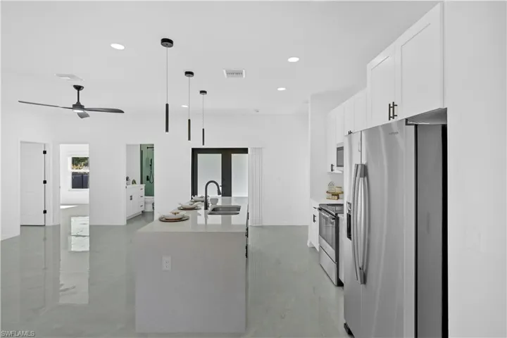 Kitchen with appliances with stainless steel finishes, white cabinets, decorative light fixtures, light stone countertops, and recessed lighting