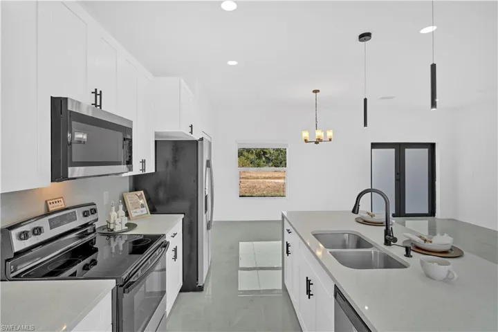 Kitchen featuring stainless steel appliances, white cabinets, light stone counters, hanging light fixtures, and concrete flooring