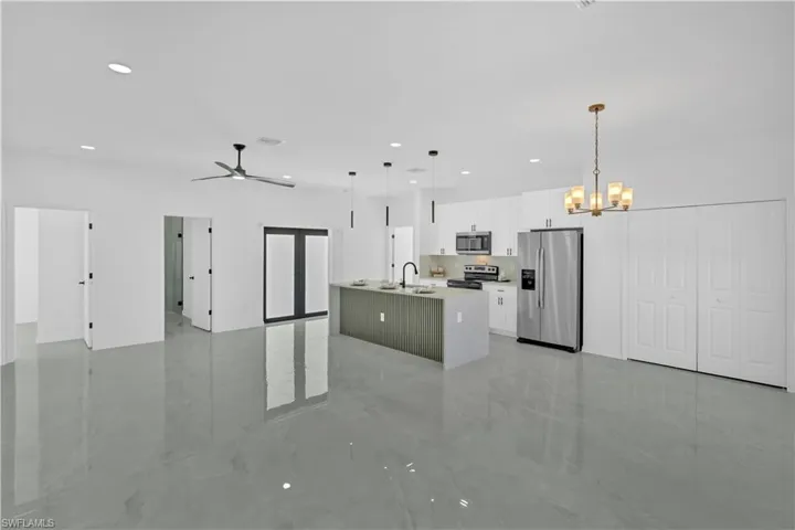 Kitchen with open floor plan, appliances with stainless steel finishes, a kitchen island with sink, white cabinetry, and hanging light fixtures
