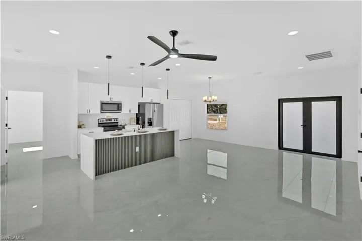 Kitchen with open floor plan, a kitchen island with sink, decorative light fixtures, white cabinets, and stainless steel appliances