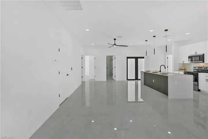Kitchen with white cabinets, appliances with stainless steel finishes, open floor plan, an island with sink, and pendant lighting