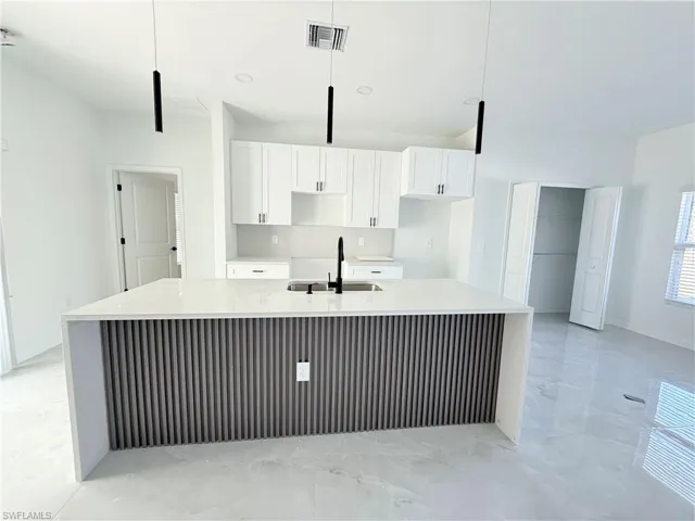 Kitchen featuring light stone counters, light marble finish floors, white cabinets, and a spacious island