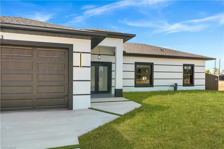 View of exterior entry featuring french doors, a yard, roof with shingles, driveway, and an attached garage