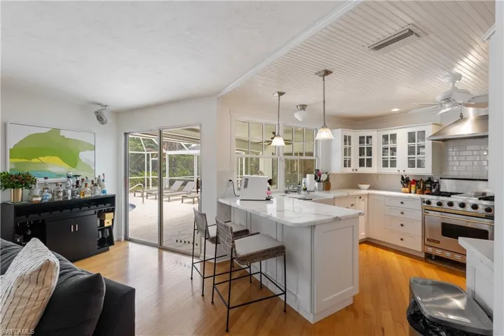 Kitchen featuring designer range, light wood-type flooring, wall chimney exhaust hood, white cabinets, and sink