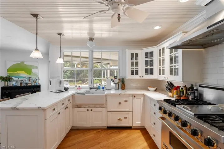 Kitchen with stainless steel stove, decorative light fixtures, wall chimney range hood, light hardwood / wood-style flooring, and tasteful backsplash