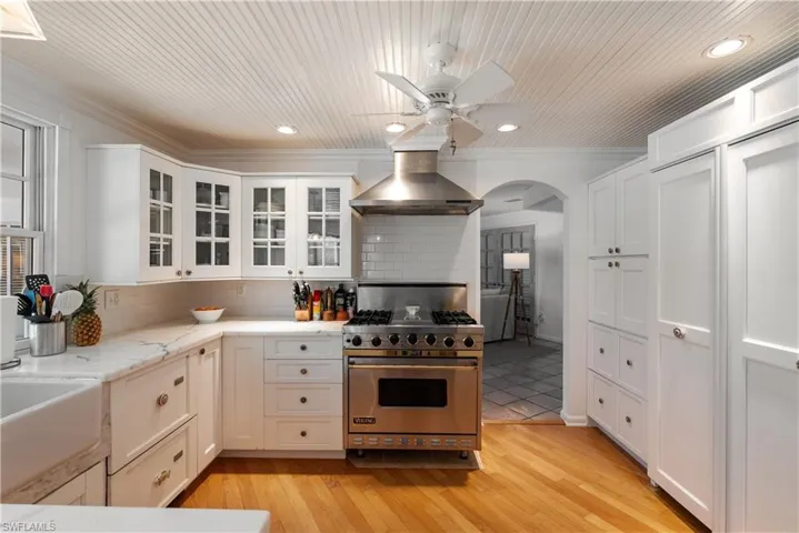 Kitchen with premium range, light hardwood / wood-style floors, ceiling fan, tasteful backsplash, and wall chimney exhaust hood