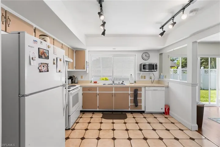 Kitchen featuring white appliances, track lighting, light floors, light countertops, and a raised ceiling