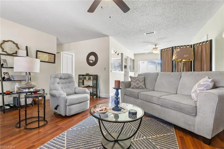 Living area with a ceiling fan, wood finished floors, and a textured ceiling