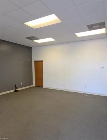 Carpeted spare room featuring a drop ceiling and baseboards