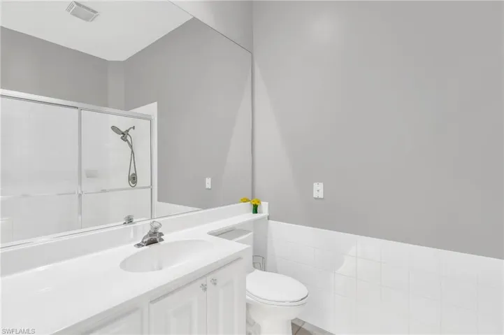 Bathroom with vanity, toilet, an enclosed shower, and tile walls