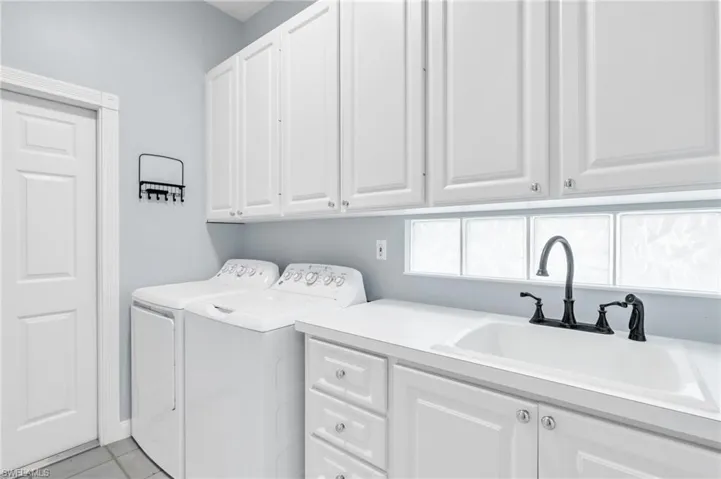 Clothes washing area with independent washer and dryer, cabinets, sink, and light tile patterned flooring