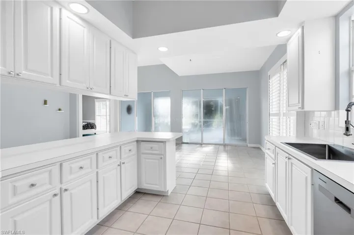 Kitchen with white cabinetry, sink, kitchen peninsula, light tile patterned flooring, and stainless steel dishwasher