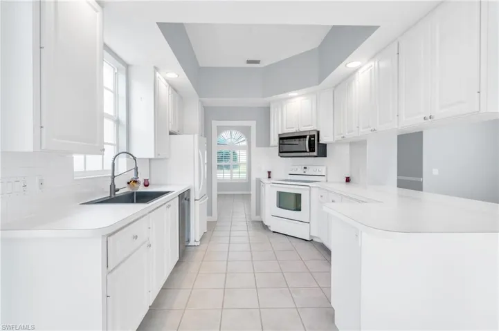 Kitchen featuring light tile patterned floors, white cabinetry, white range with electric cooktop, and sink