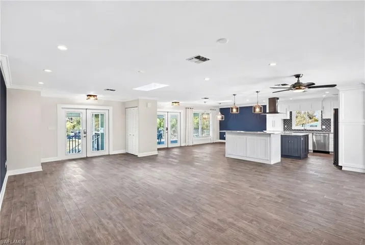 Spacious open-concept living area featuring wood-like tile flooring, recessed lighting, and multiple sets of French doors