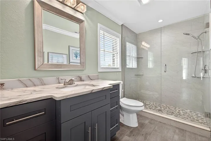 Primary bathroom featuring a dark wood-finish vanity with a light-colored stone countertop, an undermount sink, and a framed glass shower