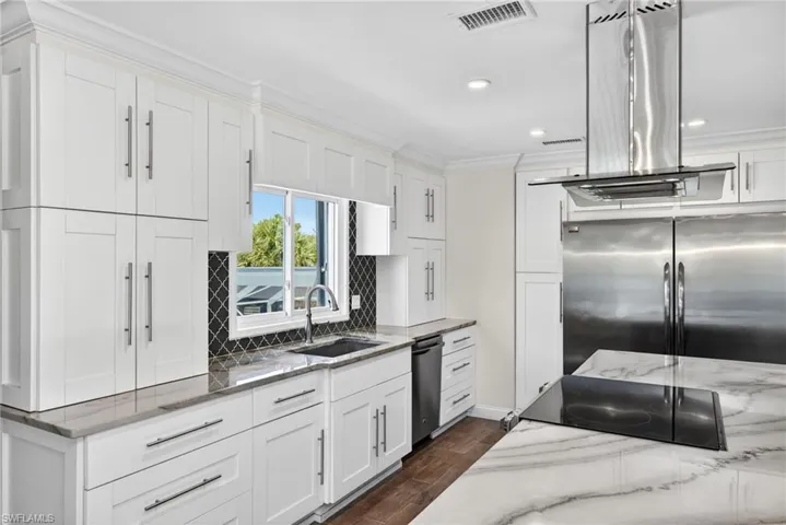 Modern kitchen featuring white shaker cabinetry,a built-in cooktop, and a range hood