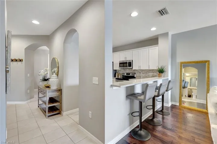 Kitchen with  breakfast/lunch  bar, kitchen island, light entry tile & LR wood-style flooring. Appliances have stainless steel finishes, and white cabinetry!