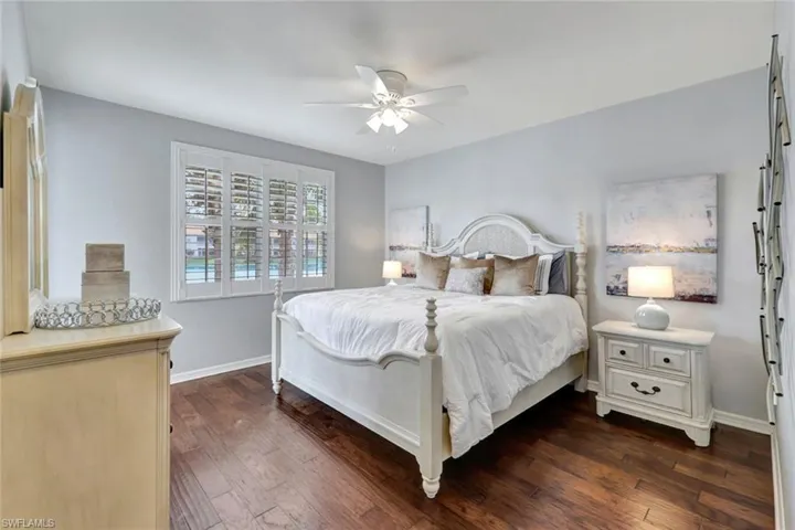 Large primary bedroom with wide lake and lanai views, lighted ceiling fan and rich, hardwood flooring