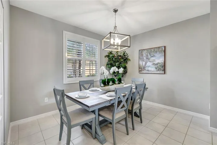 Large tiled dining space featuring plantation shuttered window and inviting chandelier