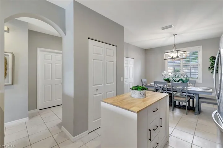 Kitchen featuring butcher block center island, pantry and closet, decorator light fixture, light tile floors, and white cabinetry.