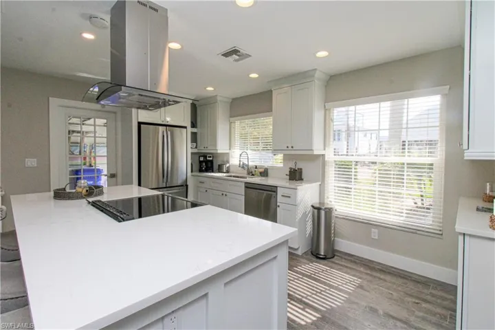 Kitchen featuring white cabinets, sink, appliances with stainless steel finishes, island range hood, and wood-type flooring