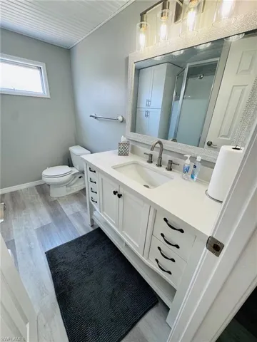 White vanity with black hardware, undermount sink, and light-tone wood-finish flooring