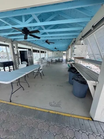 Covered outdoor entertaining area featuring a blue wood-beam ceiling, concrete flooring, and multiple ceiling fans