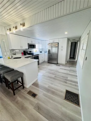 Kitchen featuring white cabinetry, stainless steel appliances, a breakfast bar, recessed lighting, and wood-finish flooring