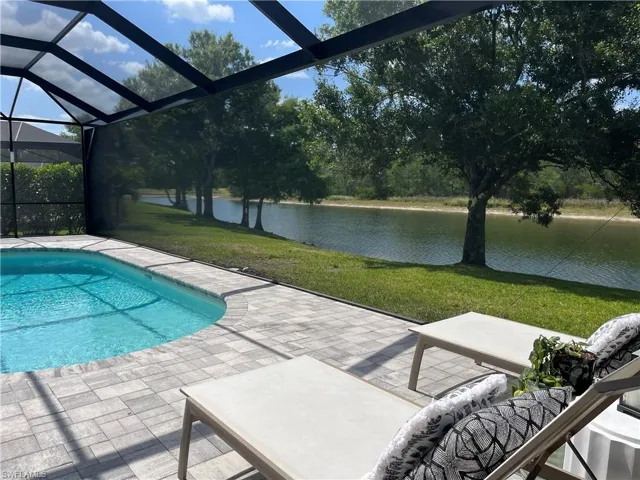 Outdoor pool with a patio area, a water view, a lanai, and a yard