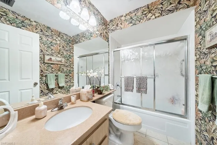 Full bathroom with vanity, combined bath / shower with glass door, tile patterned flooring, and toilet