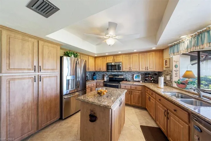 Kitchen with stainless steel appliances, a raised ceiling, tasteful backsplash, and a kitchen island