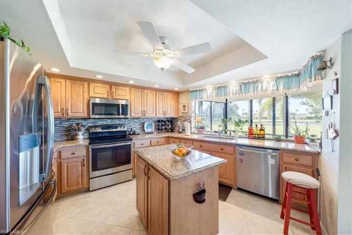 Kitchen with a raised ceiling, a kitchen island, backsplash, and stainless steel appliances