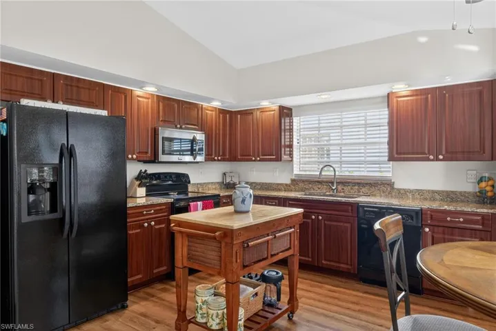 Kitchen with black appliances, lofted ceiling, light wood-style flooring, light stone countertops, and recessed lighting