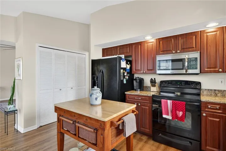 Kitchen with black appliances, light stone countertops, and light wood-type flooring