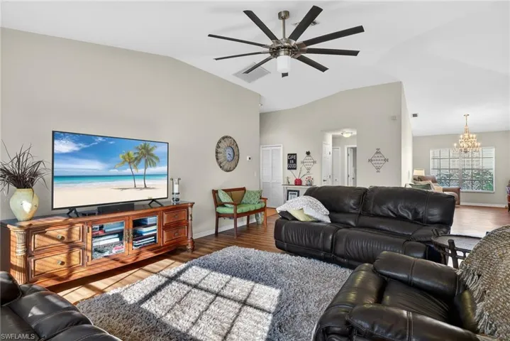 Living area with a chandelier, wood finished floors, ceiling fan, and high vaulted ceiling