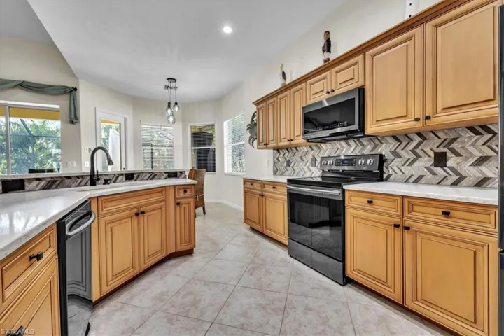 Kitchen with electric stove, stainless steel microwave, light tile patterned flooring, dishwasher, and hanging light fixtures